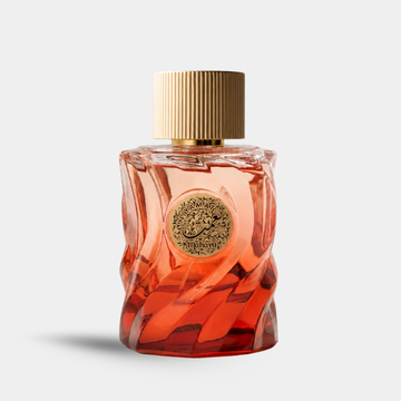 A bottle of Niyamat_Rouge Missoni Pour Homme fragrance with a sculpted, wavy transparent glass body showing a warm orange-amber liquid inside, topped with a ribbed gold cap and a circular gold logo medallion on the front, set against a light gray background.