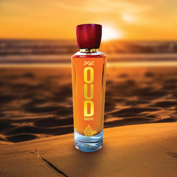 A bottle of Oud Ambari perfume standing upright on a surface with a sunset in the background.